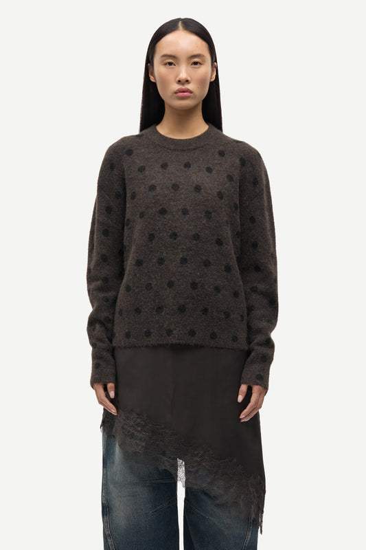 Person wearing a dark brown sweater with black polka dots on a white background
