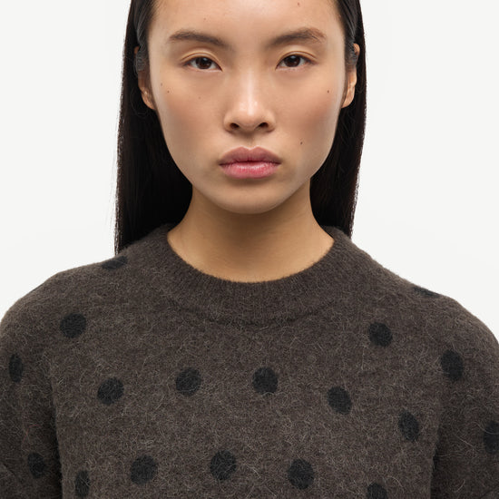 Woman wearing a dark brown sweater with black polka dots against a white background