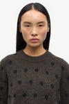 Woman wearing a dark brown sweater with black polka dots against a white background
