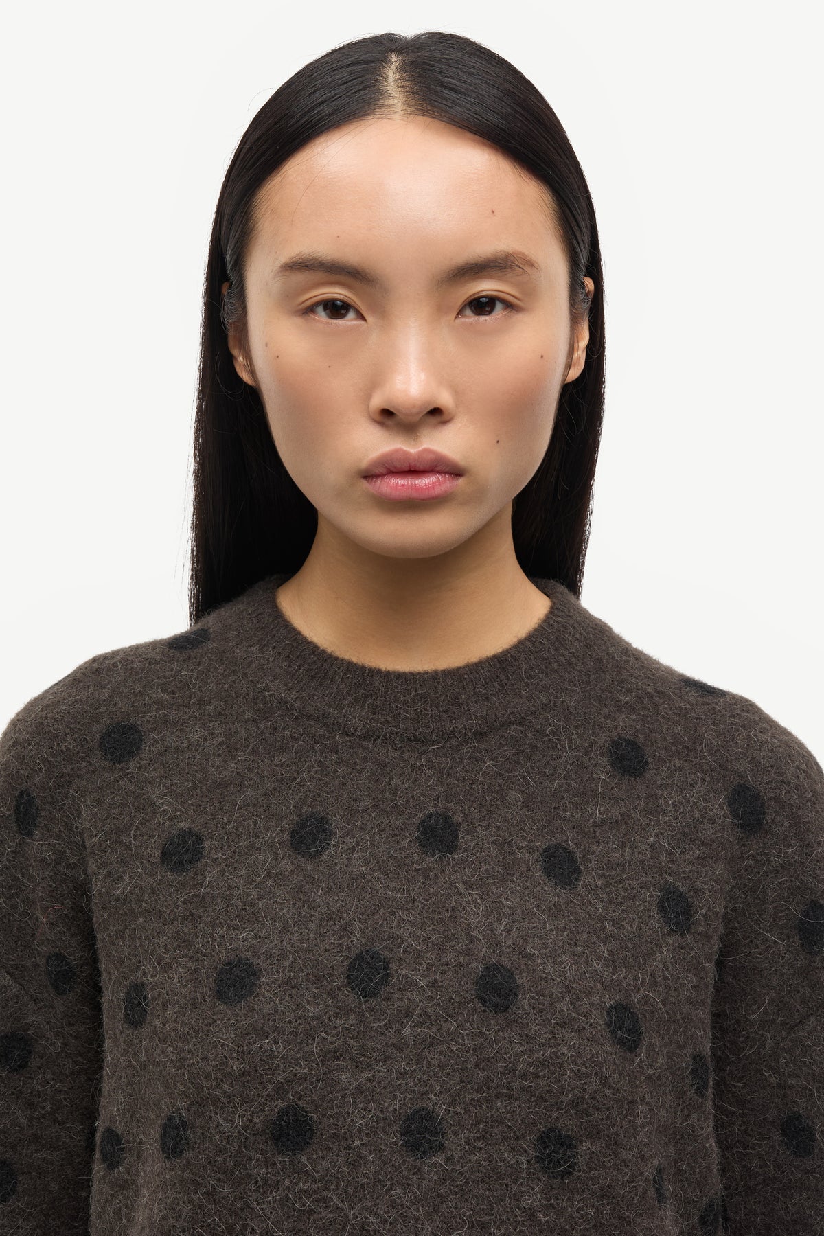 Woman wearing a dark brown sweater with black polka dots against a white background