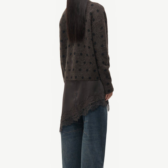Person wearing a dark patterned cardigan and jeans on a white background