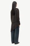 Person wearing a dark patterned cardigan and jeans on a white background
