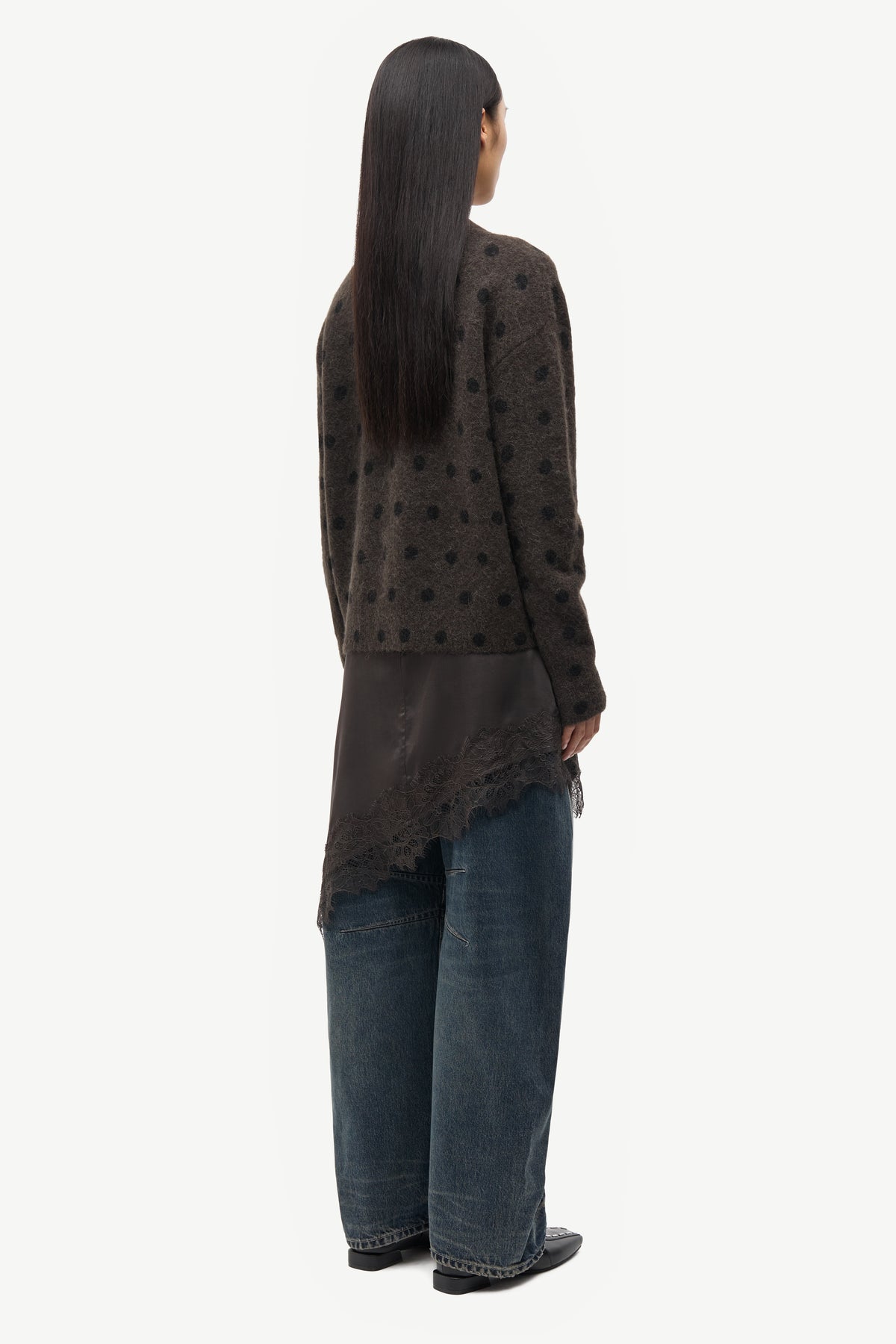 Person wearing a dark patterned cardigan and jeans on a white background