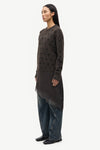 A model is shown in profile wearing a dark brown textured knit tunic with a sheer lace overlay and wide-leg blue jeans, set against a plain light gray background.