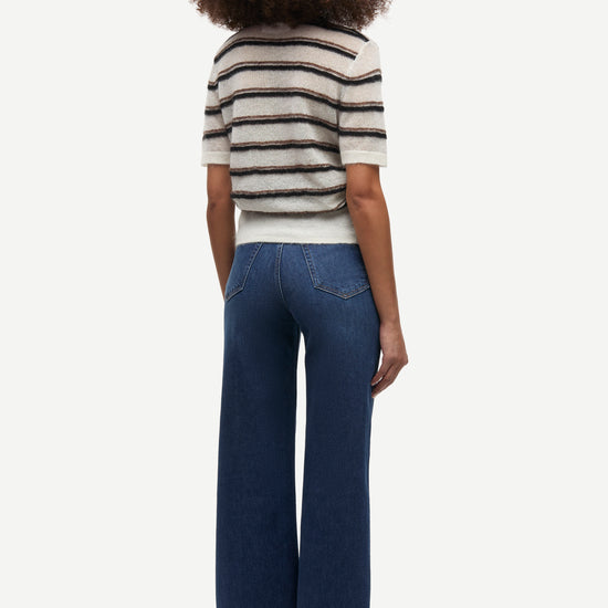 A model shown from the back wearing a short-sleeve knit top with black and white horizontal stripes and dark blue wide-leg jeans, set against a plain light gray background.