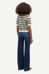 A model shown from the back wearing a short-sleeve knit top with black and white horizontal stripes and dark blue wide-leg jeans, set against a plain light gray background.