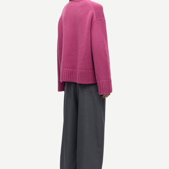 A model shown from the back wearing a magenta knit cardigan and dark gray wide-leg trousers, photographed against a solid off-white background.