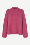 A pink ribbed knit crewneck sweater with dropped shoulders and ribbed cuffs, displayed on a clean off-white background.