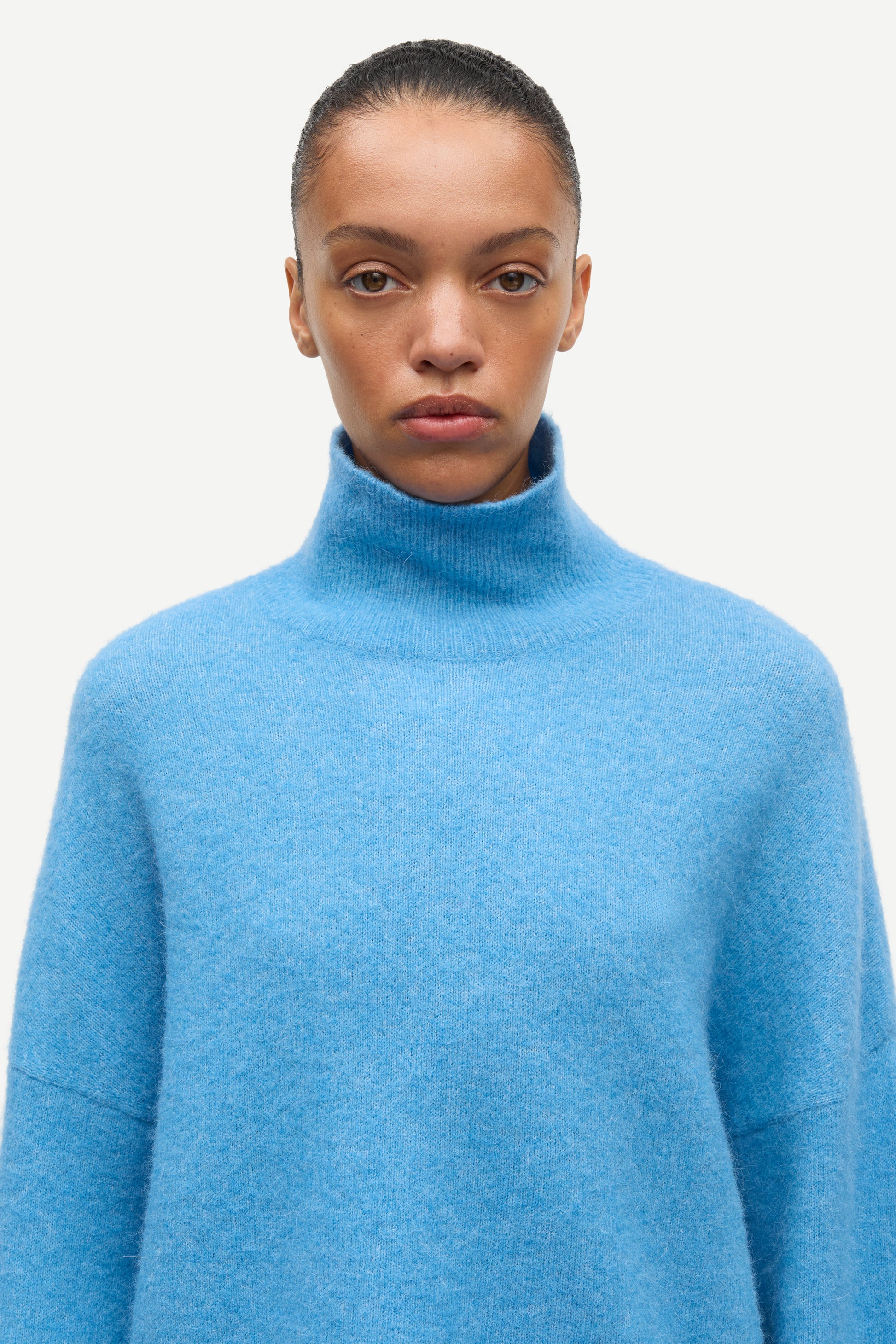 A model wearing a light blue knit turtleneck sweater against a plain off-white background.