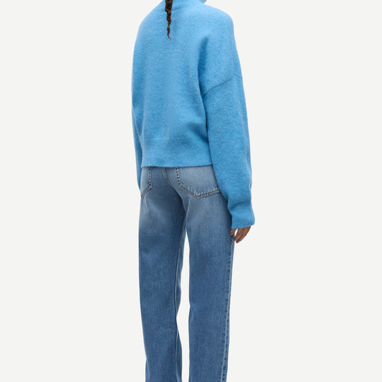 A model shown from the back wearing a light blue knit mock-neck sweater and blue jeans against a plain light gray background.