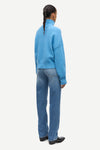 A model shown from the back wearing a light blue knit mock-neck sweater and blue jeans against a plain light gray background.