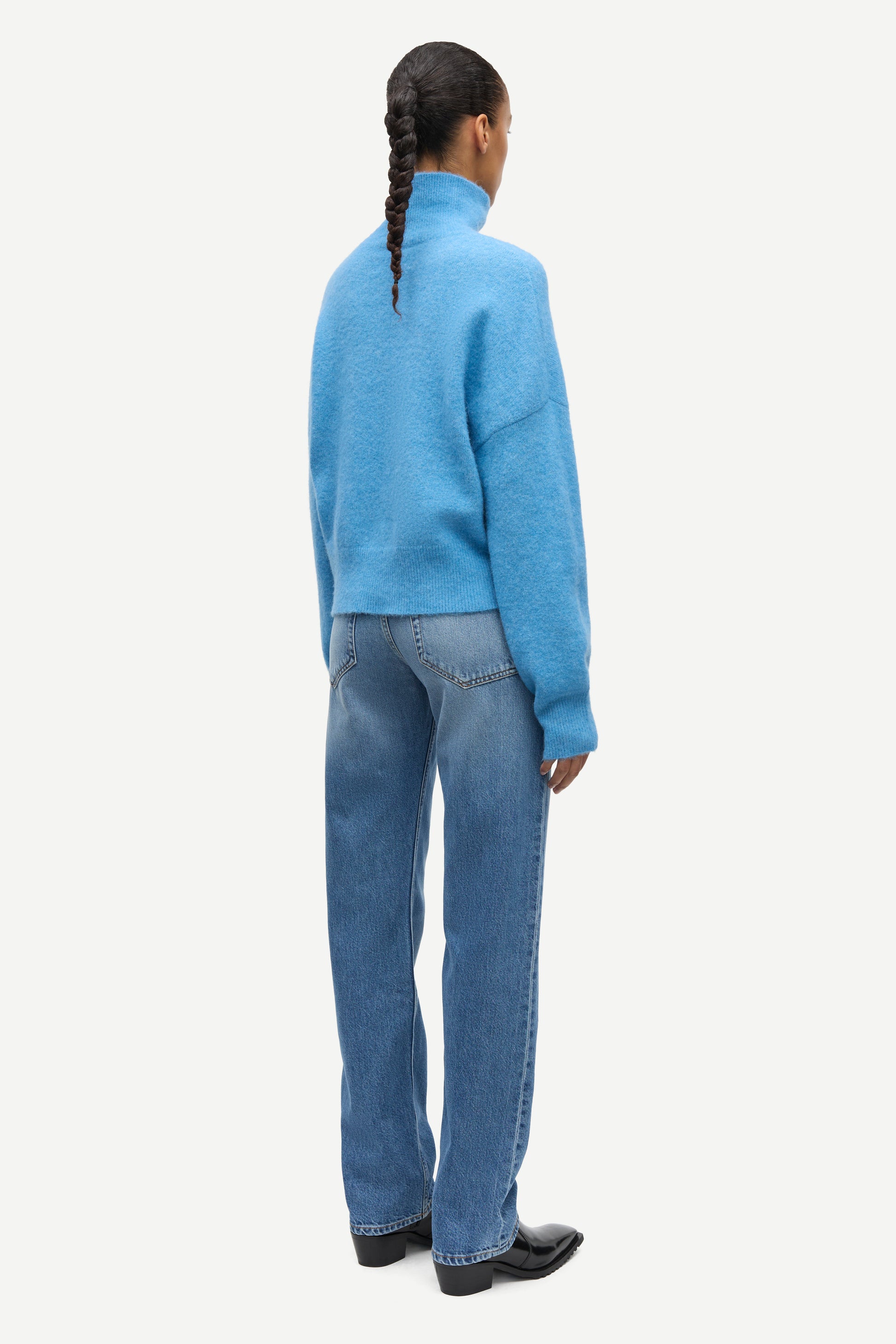 A model shown from the back wearing a light blue knit mock-neck sweater and blue jeans against a plain light gray background.