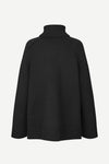 A black knit turtleneck sweater shown from the back, featuring a ribbed high collar, shoulders, cuffs, and hem, set against a plain light gray background.