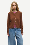 A woman modeling a brown button-up cardigan sweater over a pink top and blue jeans, photographed against a plain light gray studio background.
