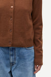 Close-up of a person wearing a brown button-front cardigan sweater with blue jeans against a plain light background.