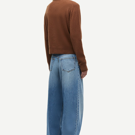 A model shown from the back wearing a brown cropped long-sleeve knit top and wide-leg light blue denim jeans, photographed against a solid off-white background.