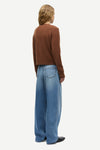 A model shown from the back wearing a brown cropped long-sleeve knit top and wide-leg light blue denim jeans, photographed against a solid off-white background.