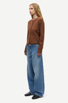 A woman modeling a brown long-sleeve knit cardigan and wide-leg blue jeans against a plain light gray studio background.