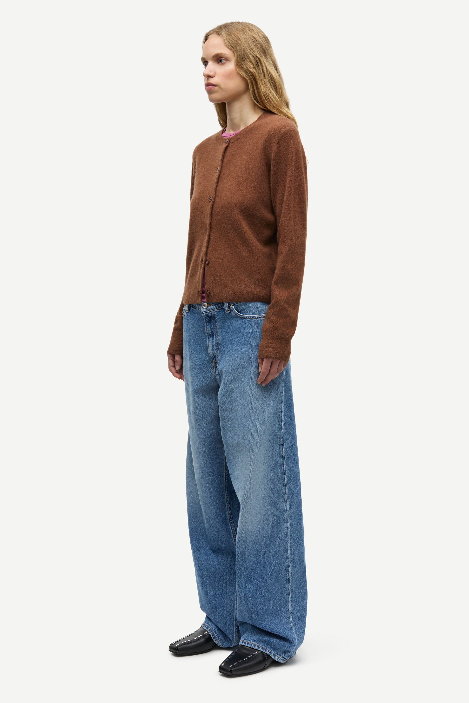 A woman modeling a brown long-sleeve knit cardigan and wide-leg blue jeans against a plain light gray studio background.