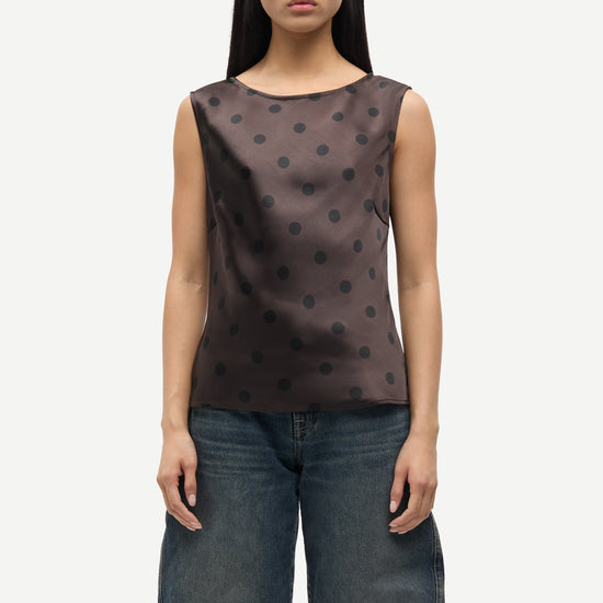 Woman wearing a brown sleeveless top with black polka dots and blue jeans on a white background
