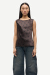 Woman wearing a brown sleeveless top with black polka dots and blue jeans on a white background