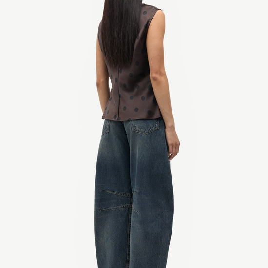 Person wearing a sleeveless patterned top and dark blue jeans on a white background