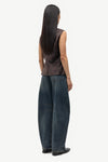 Person wearing a sleeveless patterned top and dark blue jeans on a white background