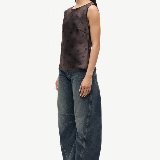 Woman wearing a patterned top and jeans on a white background
