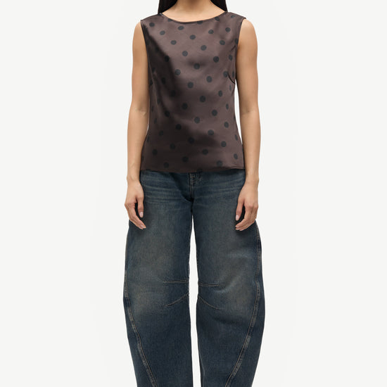 Woman wearing a brown polka dot top and dark blue jeans on a white background