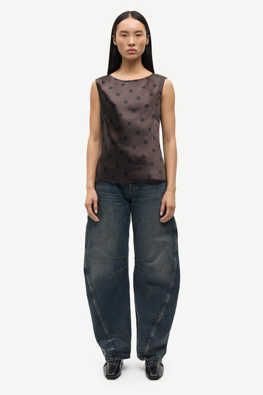Woman wearing a brown polka dot top and dark blue jeans on a white background