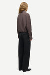 A model shown from the back wearing a dark brown textured long-sleeve shirt and black wide-leg trousers, standing against a light gray background.