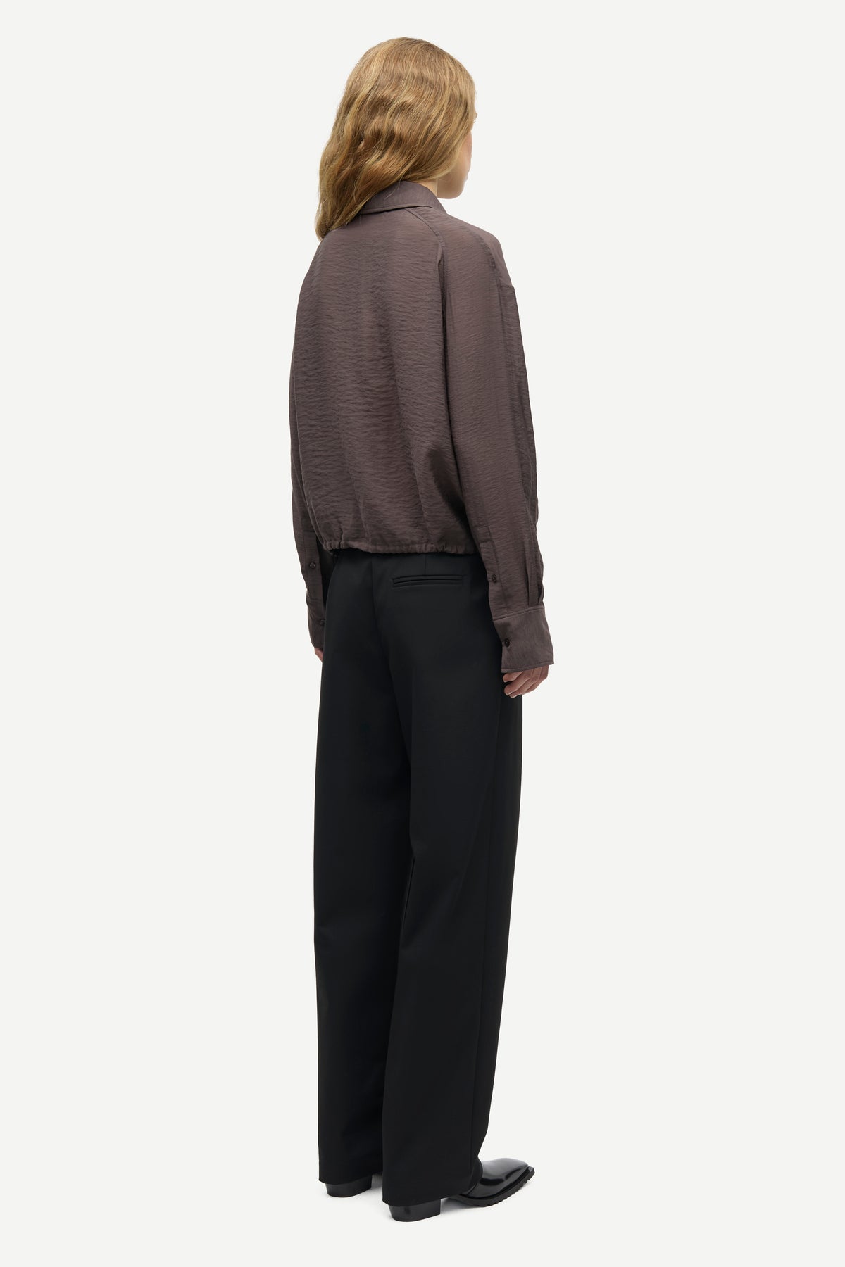 A model shown from the back wearing a dark brown textured long-sleeve shirt and black wide-leg trousers, standing against a light gray background.