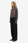 A model shown in profile wearing a dark brown textured long-sleeve button-up shirt and black wide-leg trousers against a light gray background.