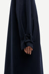 Close-up of a dark navy wool coat with a wide cuff featuring a decorative button detail, worn by a model whose hand is visible.