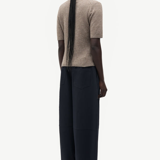 A model shown from the back wearing a beige short-sleeve knit top and dark navy wide-leg trousers, set against a plain light gray background.