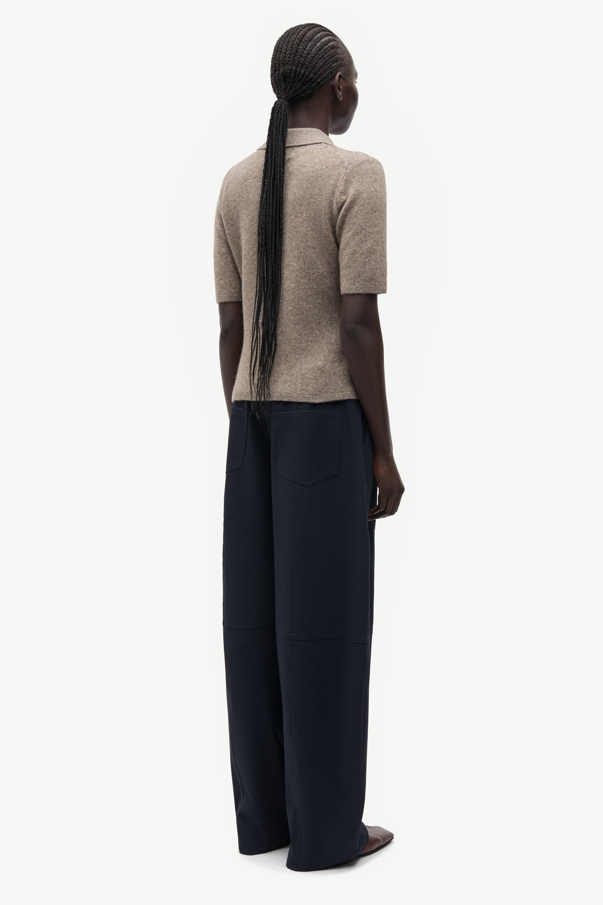 A model shown from the back wearing a beige short-sleeve knit top and dark navy wide-leg trousers, set against a plain light gray background.