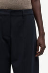 Close-up of a person wearing dark navy pinstriped trousers, showing the waistband, front pocket, and hand against a light neutral background.
