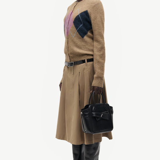 woman wearing brown pink and blue argyle cardigan holding bag on white background