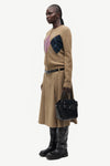 woman wearing brown pink and blue argyle cardigan holding bag on white background