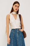 Woman wearing a white sleeveless top and blue jeans with a brown leather bag on a plain background