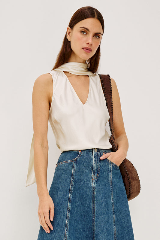 Woman wearing a white sleeveless top and blue jeans with a brown leather bag on a plain background