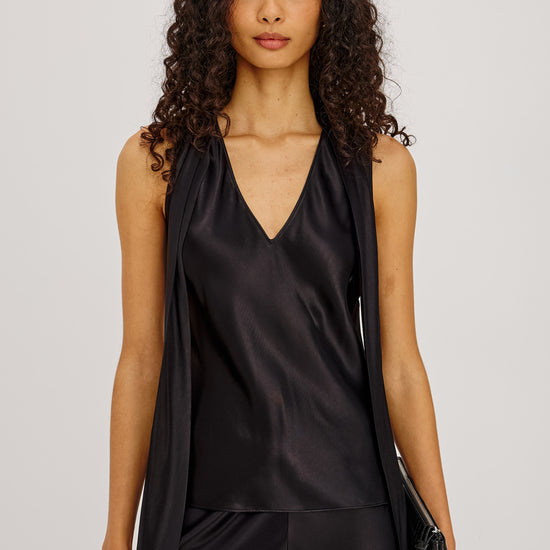 Woman wearing a black sleeveless top and pants with a clutch against a light gray background