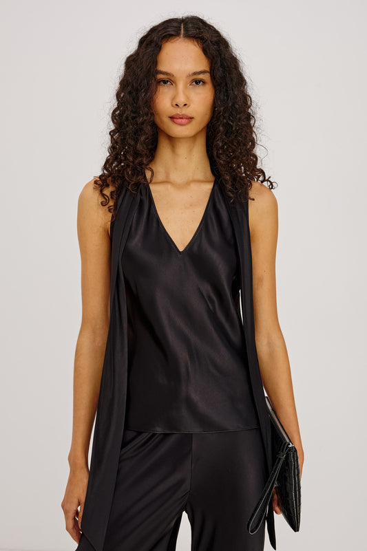 Woman wearing a black sleeveless top and pants with a clutch against a light gray background