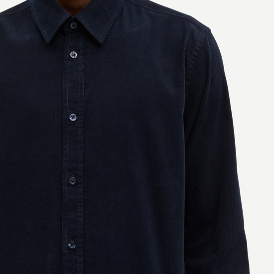 Close-up of a person wearing a dark navy long-sleeve button-up shirt against a light gray background.