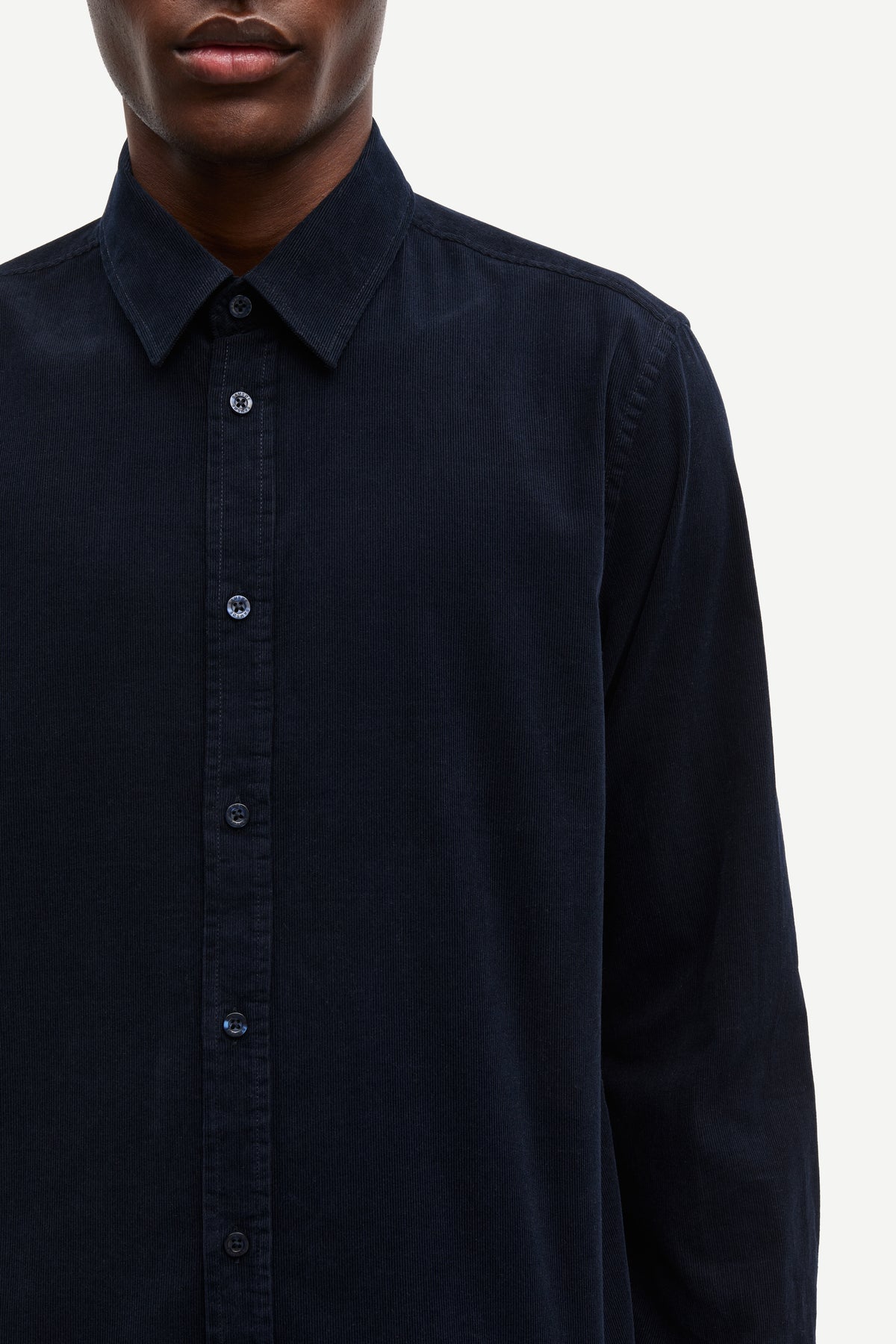 Close-up of a person wearing a dark navy long-sleeve button-up shirt against a light gray background.
