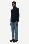 Man wearing a dark blue shirt and light blue jeans on a white background