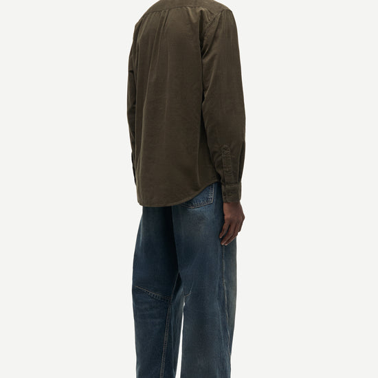 A man shown from the back wearing an olive brown long-sleeve button-up shirt, blue jeans, and brown shoes against a light gray background.