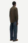 A man shown from the back wearing an olive brown long-sleeve button-up shirt, blue jeans, and brown shoes against a light gray background.