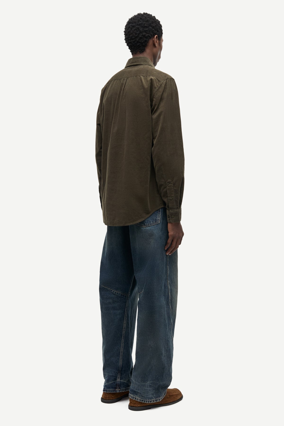 A man shown from the back wearing an olive brown long-sleeve button-up shirt, blue jeans, and brown shoes against a light gray background.