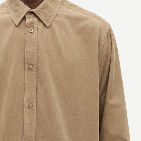 Close-up of a man wearing a tan long-sleeve button-down shirt with a pointed collar and matching buttons, shown against a plain light background.